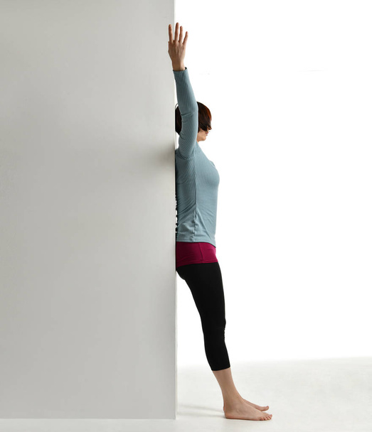 Woman exercising doing postnatal workout. Female fitness instructor stretching her spine near wall in gym work out exercises - Fotografie, Obrázek