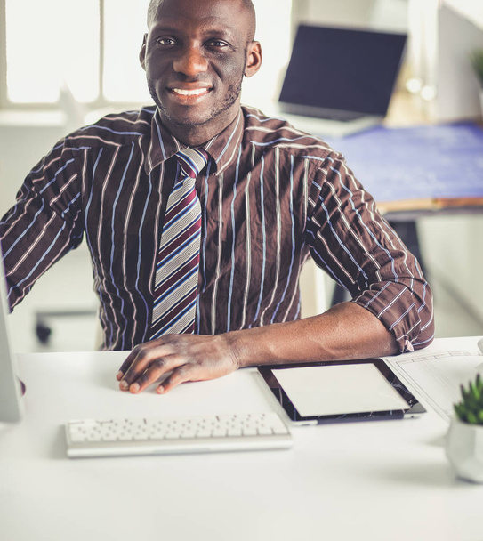 Handsome afro american businessman in classic suit is using a laptop and smiling while working in office - Фото, зображення