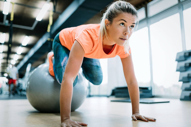 Young attractive woman doing push ups using ball in gym - 写真・画像