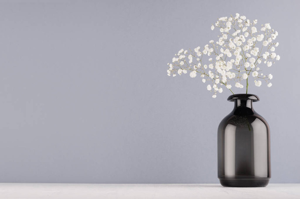 Modern elegáns lakberendezés fekete átlátszó sima üveg váza, a kis virágok táblán pasztell szürke színű fal és fehér fa. - Fotó, kép