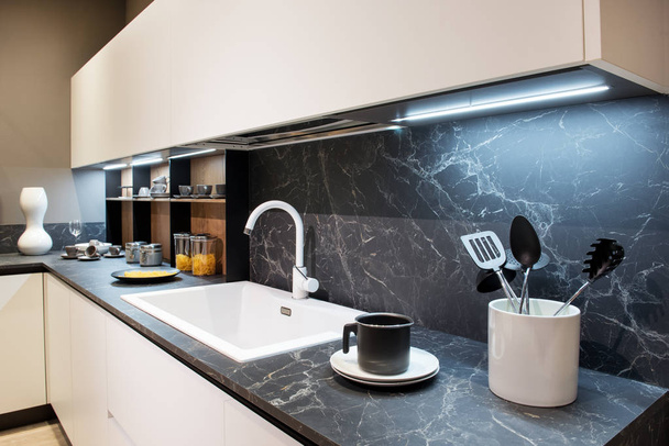 Marmor-Effekt-Küchentheke mit Utensilien und einer weißen rechteckigen Spüle unter Wandschränken und Spritzboden - Foto, Bild