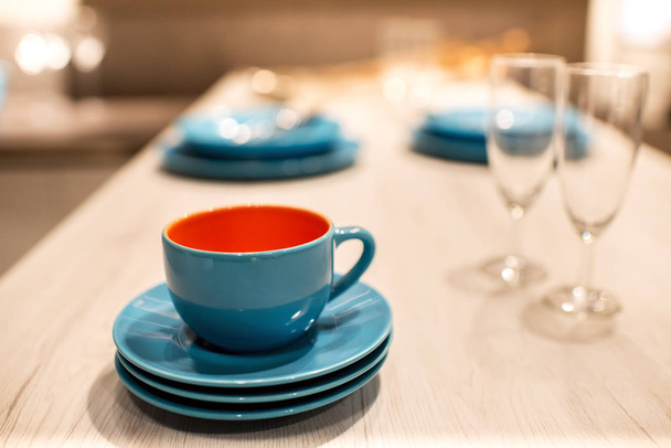 Blue stoneware or ceramic cup and saucers on a rustic wooden kitchen table with champagne flutes in a shallow dof view - Photo, Image
