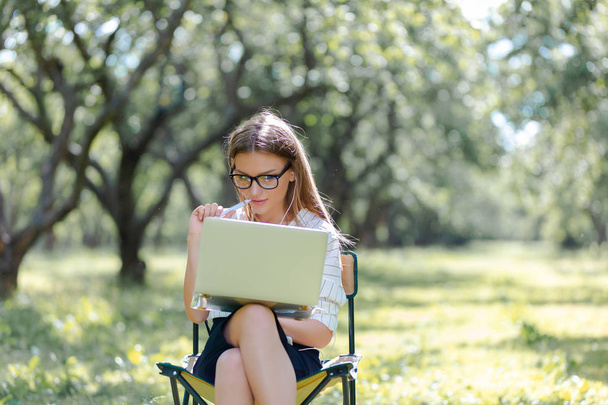 Woman with a laptop in the Park sitting on a folding chair - Foto, afbeelding