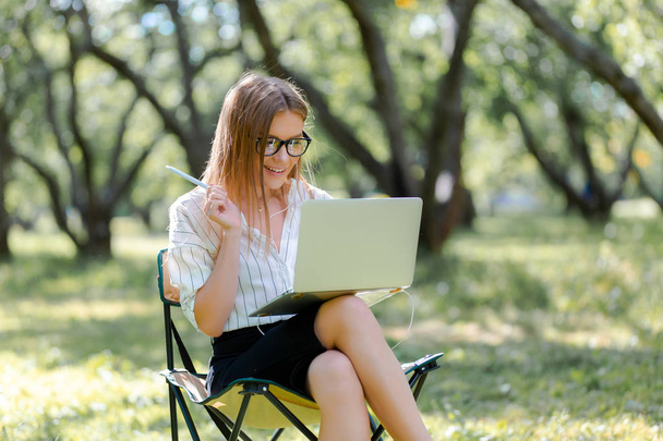 Donna con un computer portatile nel parco seduta su una sedia pieghevole
 - Foto, immagini
