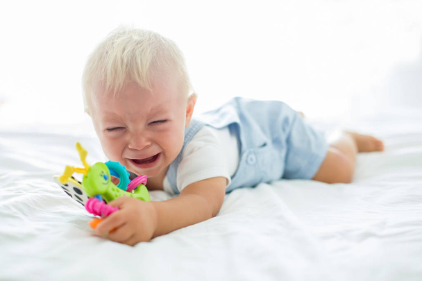 Toddler baby boy, playing with dummy, crying unhappy for the pacifier in children bedroom - Fotó, kép
