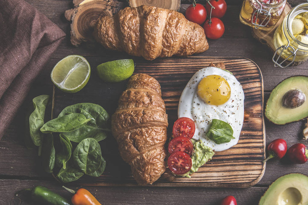 croissant with guacamole avocado, fried egg and tomato, spinach leaves. vegetarian dish - Photo, Image