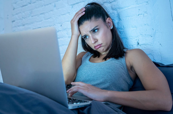 Tired attractive young woman working and surfing on the internet with computer on the sofa at home late at night in internet addiction and overwork concept. - Фото, зображення