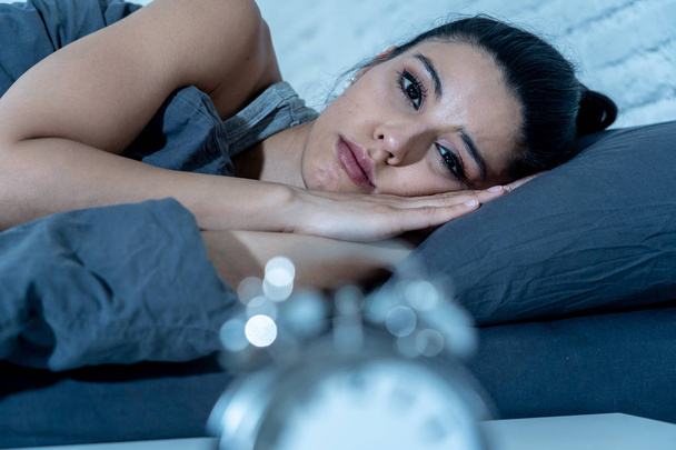 Sleepless and desperate beautiful latin woman awake at night not able to sleep looking at clock suffering from insomnia in sleep disorder concept. - Fotoğraf, Görsel