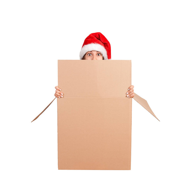 Järkyttynyt nainen jouluhatussa istuu isosta lahjapakkauksesta ja kurkkii tyhjän laatikon reunan yli. eristetty valkoisella pohjalla
. - Valokuva, kuva