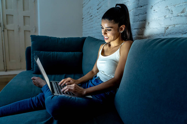 Feliz muito jovem latina usando laptop surf na internet e redes sociais sentado no sofá acolhedor em casa em tecnologia estilo de vida comunicação e conceito de pessoas
. - Foto, Imagem