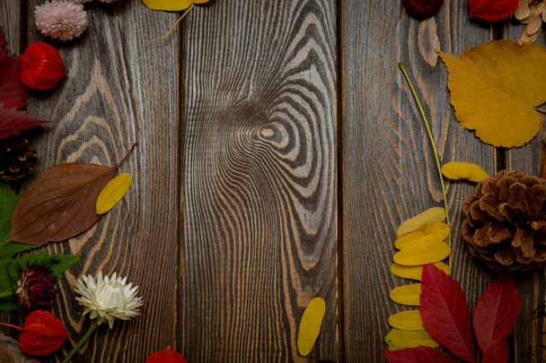 Autumn background. Bright orange berries, very flowers and leaves on a brown wood background. Background for autumn holidays and thanksgiving day. - Photo, Image