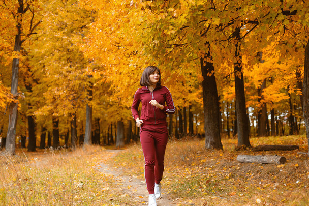 Portrait of young woman in fall forest. Brunette woman in autumn park makes a run and warm up. Sports lifestyle - Fotoğraf, Görsel