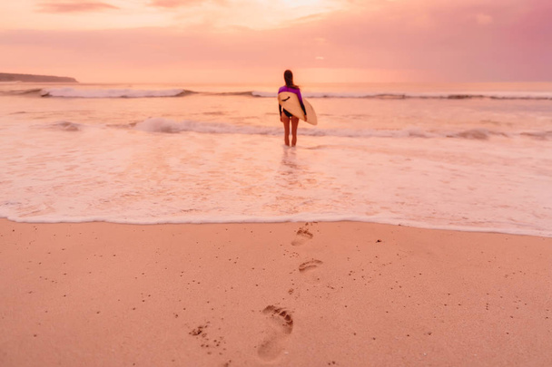 Surf girl con tabla de surf ir al surf. Mujer surfista en una playa al atardecer o al amanecer
. - Foto, imagen