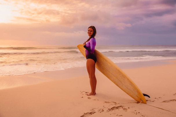 Серфінг дівчина з дошкою для серфінгу, яка отруює пляж на заході сонця або сході сонця
. - Фото, зображення