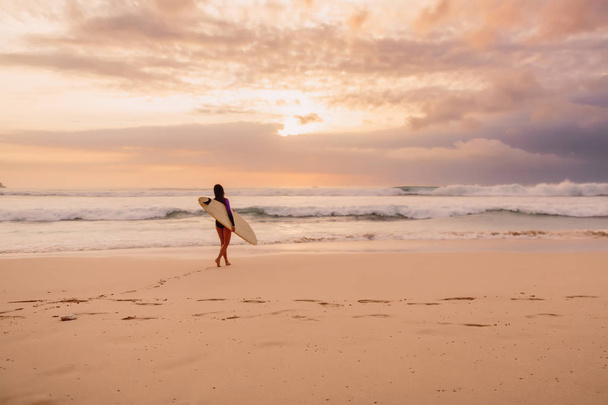 Surf girl go to ocean for surfing. Surfer woman on a beach at sunset - Φωτογραφία, εικόνα