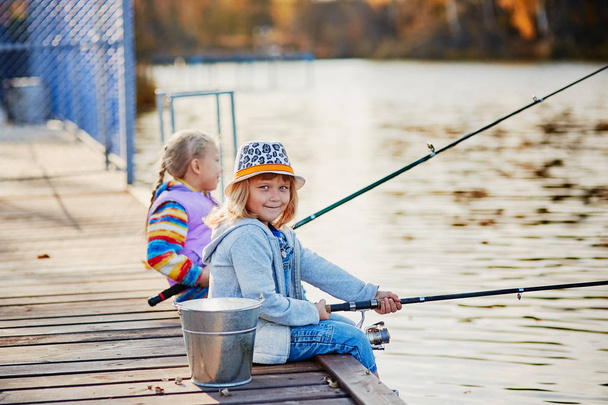 Little girls fishing on the lake, sitting on a wooden pontoon. - Φωτογραφία, εικόνα