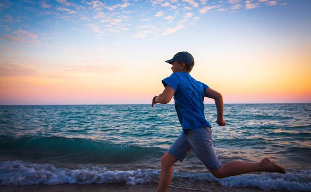 Chłopiec biegną na tropikalnej plaży o zachodzie słońca - Zdjęcie, obraz