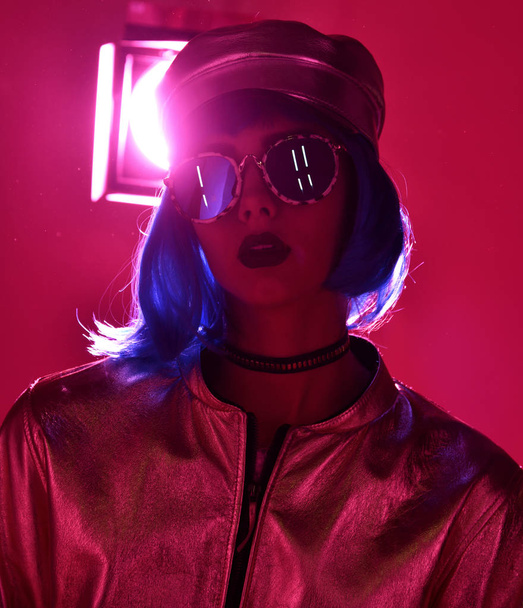 woman in street style fashion winter concept wearing gold hat cap and round sunglasses in pink neon light - Foto, immagini