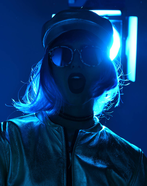 beautiful hipster woman in street style fashion autumn concept wearing round sunglasses in blue neon light - Photo, image