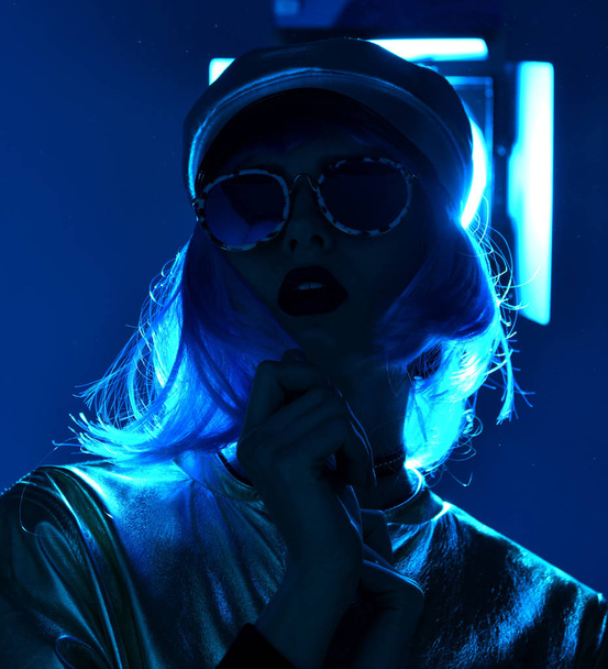 beautiful hipster woman in street style fashion autumn concept wearing round sunglasses in blue neon light - Photo, image