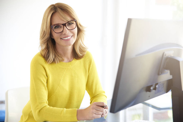Πορτρέτο του ελκυστική χαμογελώντας επιχειρηματίας συνεδρίαση μπροστά από το lap-top και κοιτάζοντας κάμερα ενώ εργάζονται σε υπολογιστή.  - Φωτογραφία, εικόνα