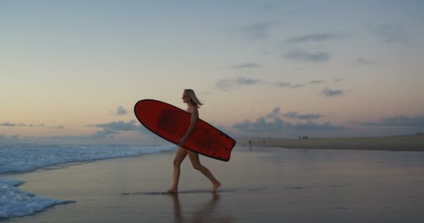 Вид збоку Кадри красивої молодої жінки в купальнику, що йде на пляжі і в море, переносячи серфінг. Дівчина має світле волосся і дуже спортивне. У повільному русі
. - Кадри, відео