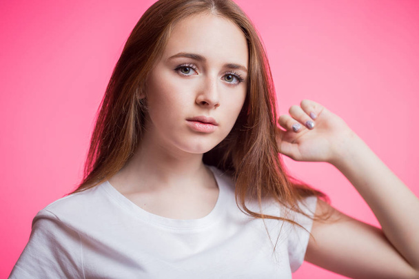 Horizontal closeup portrait of a young ginger girl with natural beauty. clean skin, long eyelashes over pink background. A woman in a white t-shirt looking at the camera - Photo, image