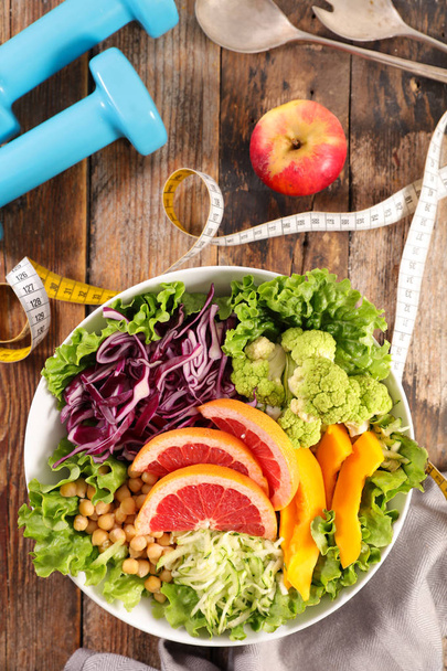 Healthy food concept, mixed vegetarian salad, centimeter tape and dumbbells - Photo, image