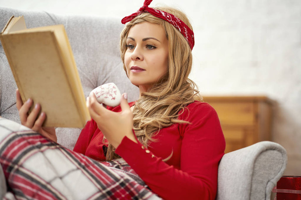 Genç güzel kadın Noel zamanı sırasında paket ve çay ile bir koltuk bir kitapta okuma - Fotoğraf, Görsel
