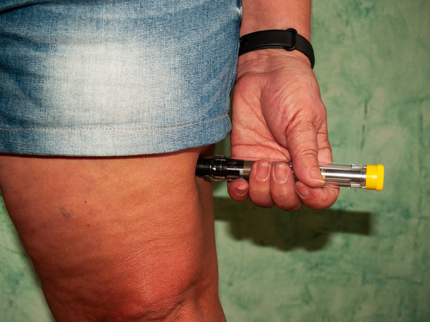 Una mujer alérgica inyectándose una inyección de adrenalina en el muslo
 - Foto, Imagen