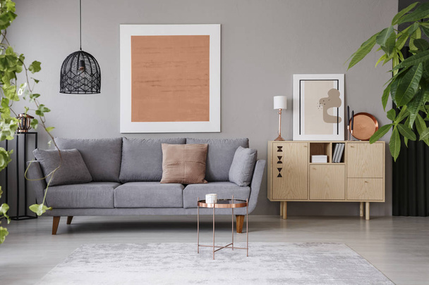 Real photo of a cozy living room interior with a grey sofa, painting, retro cupboard and plants - Fotó, kép