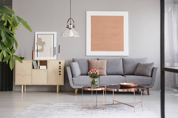 Large painting on a gray wall above an elegant sofa with cushions in a stylish living room interior with copper furniture - Fotó, kép