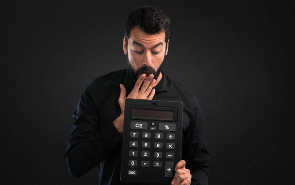 Bir hesap makinesi siyah arka plan üzerine tutarak sakallı yakışıklı adam - Fotoğraf, Görsel
