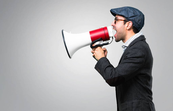 Handsome modern man with beret and glasses holding a megaphone on grey background - Photo, image