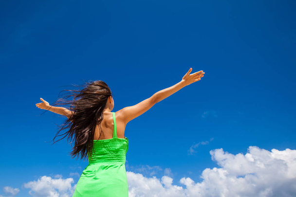 Young woman with raised hands over blue sky background - 写真・画像