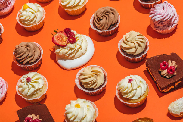 Kleurrijke cupcakes in rijen op een oranje achtergrond. Zoete smakelijke desserts. - Foto, afbeelding