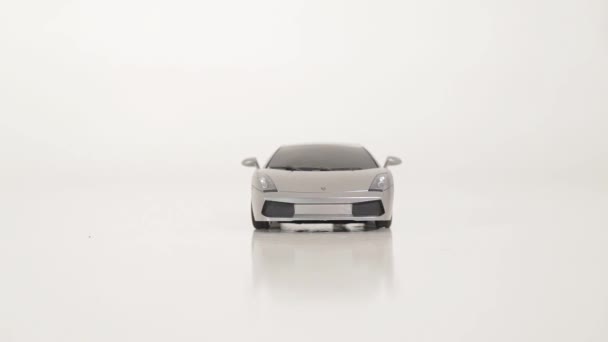 graues Plastik-Spielzeugauto wird von Männerhand auf weißem Boden aufgegriffen - Filmmaterial, Video