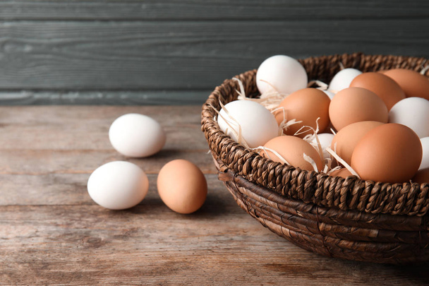 Basket with raw chicken eggs on wooden table - Фото, зображення