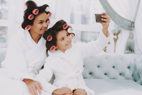 Little Lady with Curlers. Mother and Daughter in Spa. Consept Beauty Salon. Beautiful Little Lady. Beautiful Face. Woman and Happy Child. Woman with Curlers. Doing Selfie. Blue Sofa in Spa Salon. - Foto, Imagem