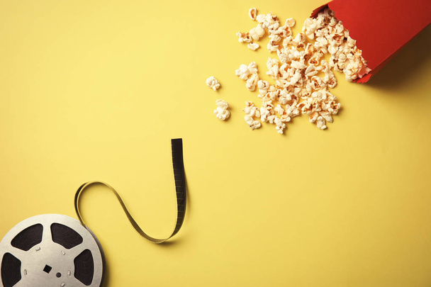 Tasty popcorn and film reel on color background, top view. Cinema snack - Photo, image