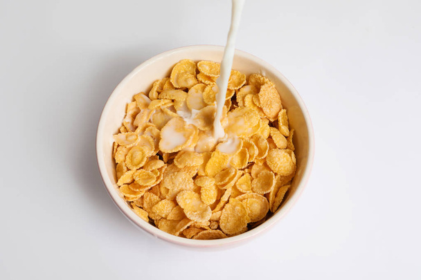 Milk pouring into bowl with crispy cornflakes on white background - Photo, image