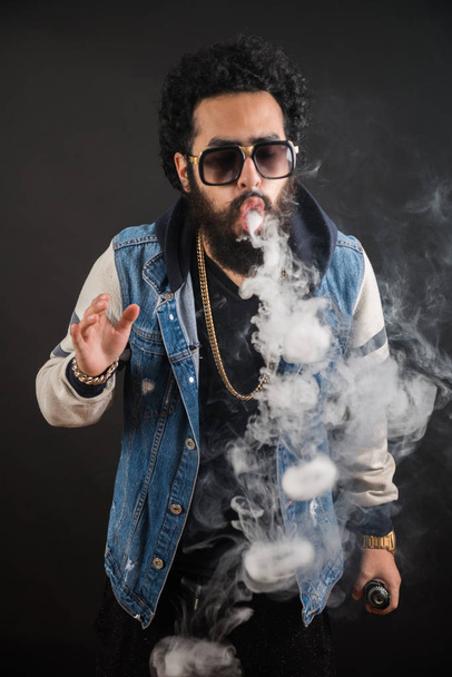 Vaping man holding a mod. A cloud of vapor. Black background. Vaping an electronic cigarette with a lot of smoke. - Foto, Imagem
