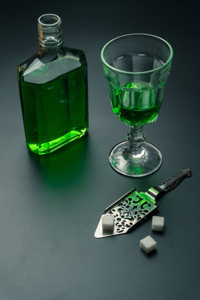 a glass of absinthe, a stainless steel slotted spoon with the sugar cubes and the absinthe bottle on the table - Zdjęcie, obraz