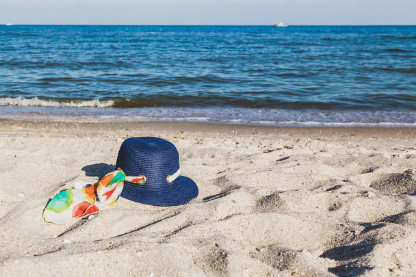 Nuevo sombrero de playa elegante con una cinta brillante en la arena contra el telón de fondo de las olas del mar
 - Foto, imagen