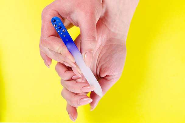 Kobieta manicure paznokci szklanym pilnikiem na żółtym tle - Zdjęcie, obraz