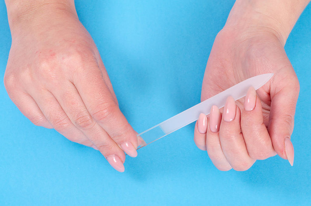Woman doing a manicure with a glass nail file on a blue background - Photo, Image