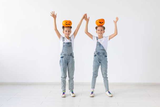 Halloween, dzieci i zabawy koncepcja - siostry szczęśliwy wesoły bliźniaków, stojąc z jack-o-lantern na głowach na białym tle. - Zdjęcie, obraz