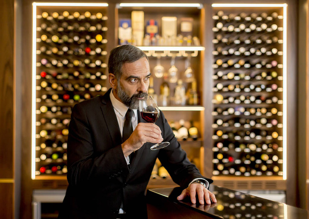 Красивый зрелый мужчина пробует бокал красного вина
 - Фото, изображение