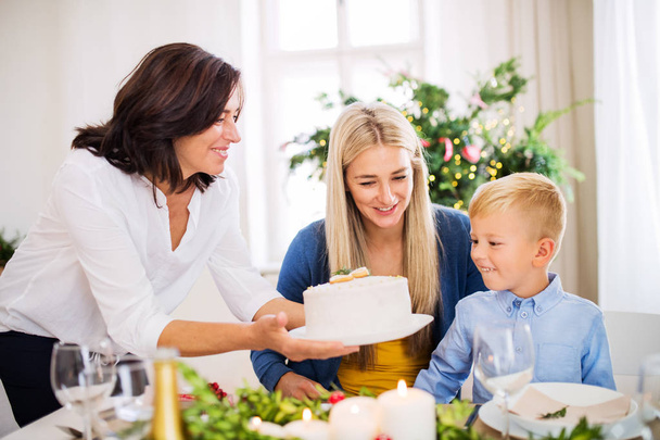 Ένα μικρό αγόρι με μητέρα βλέπει γιαγιά βάζοντας μια τούρτα στο τραπέζι, Χριστούγεννα. - Φωτογραφία, εικόνα
