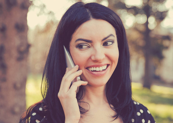 Beautiful ethnic woman having phone call while smiling and standing outdoors looking away - Foto, Imagem